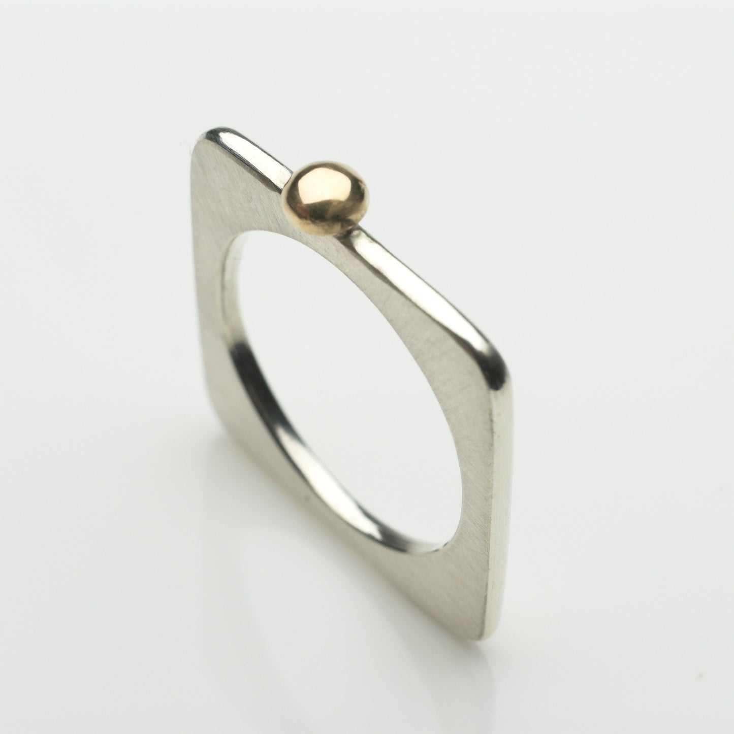 A square ring in silver with a gold ball.