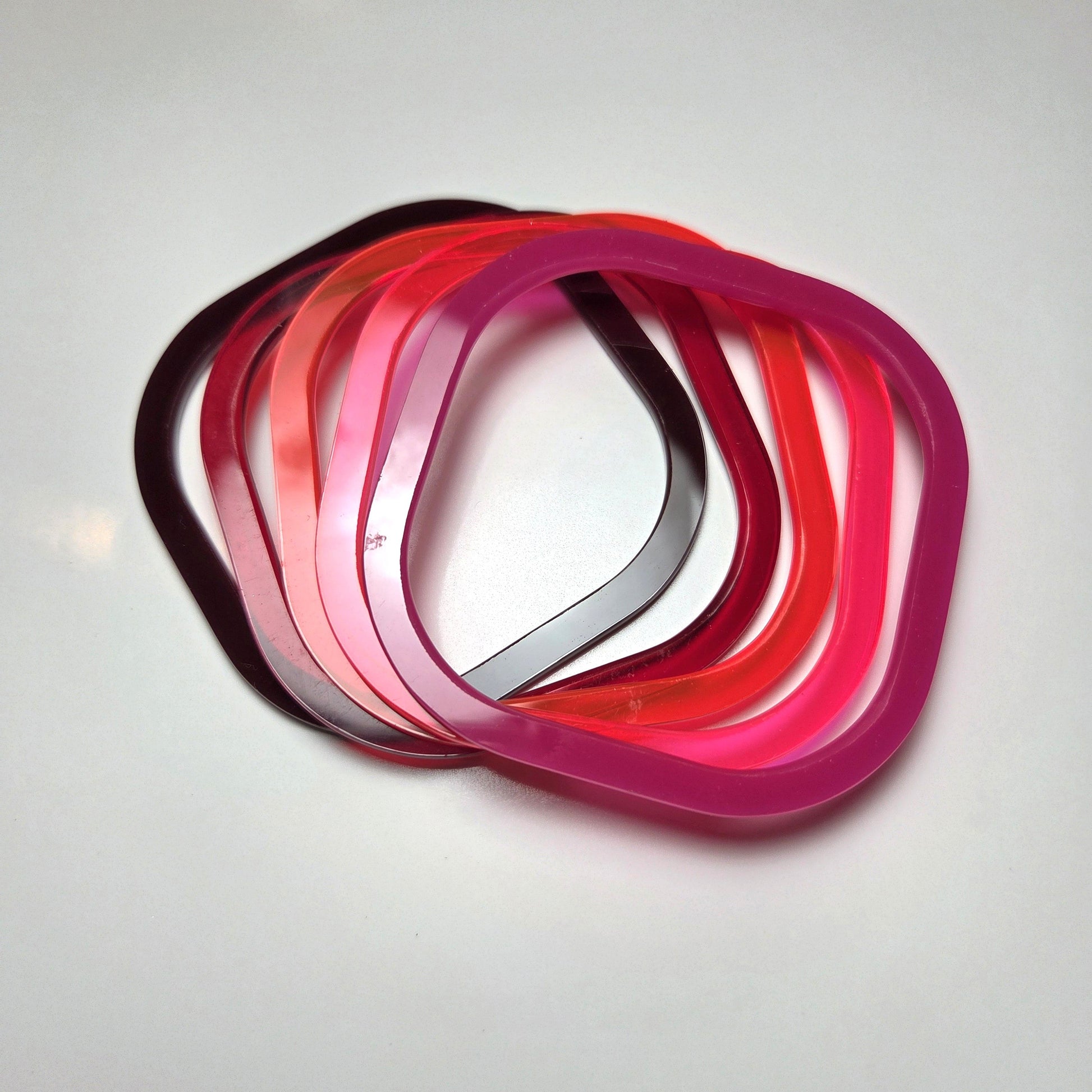 Stack of red acrylic bangles. From left to right : chocolate brown, dark red, Mars red, fluorescent pink, pink  . barbaraspence.co.uk