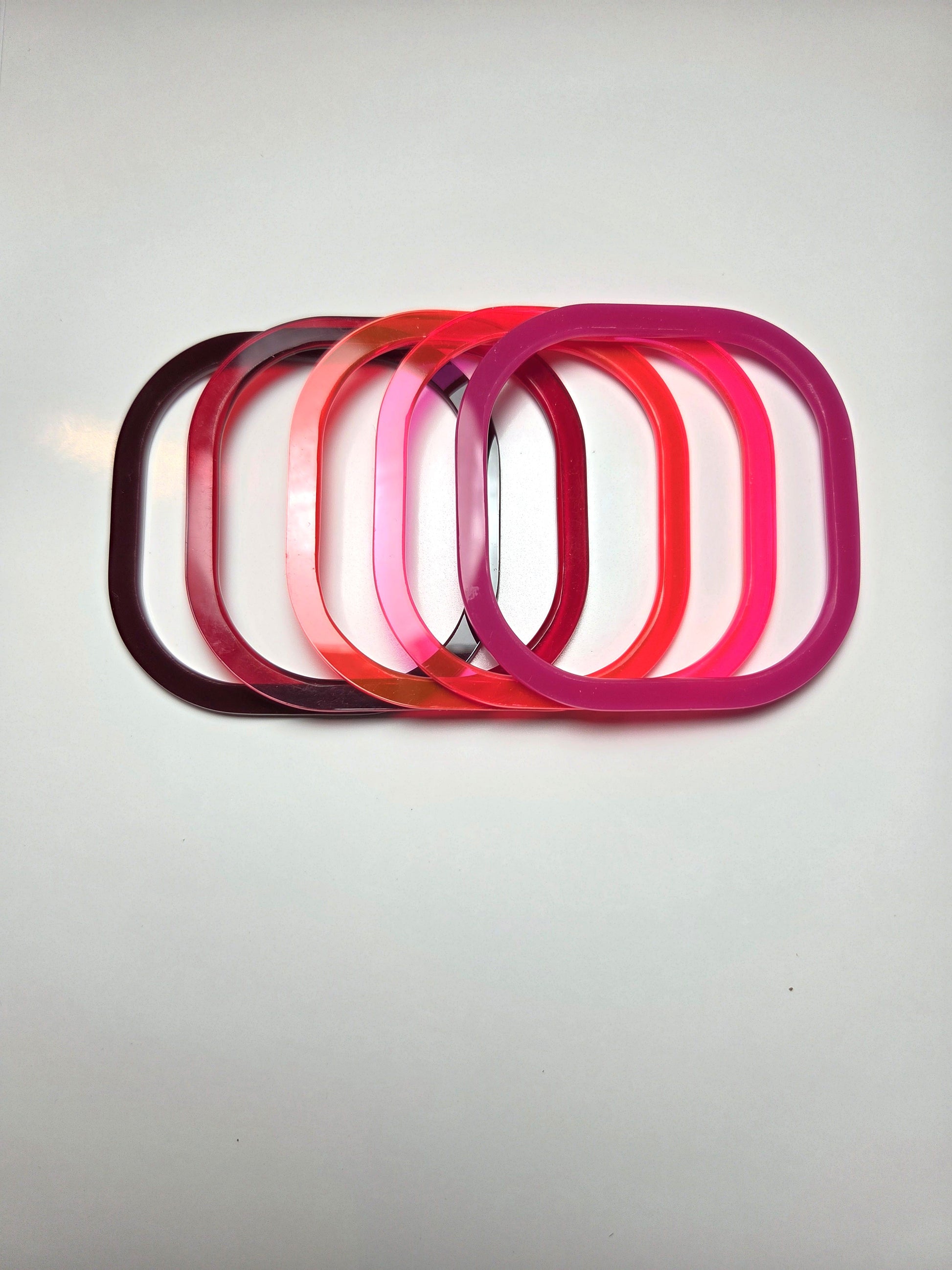Stack of red acrylic bangles. From left to right : chocolate brown, dark red, Mars red, fluorescent pink, pink  . barbaraspence.co.uk