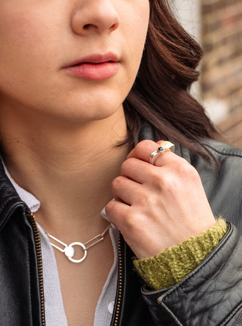 Silver necklace with rectangular links and decorative orbit feature.