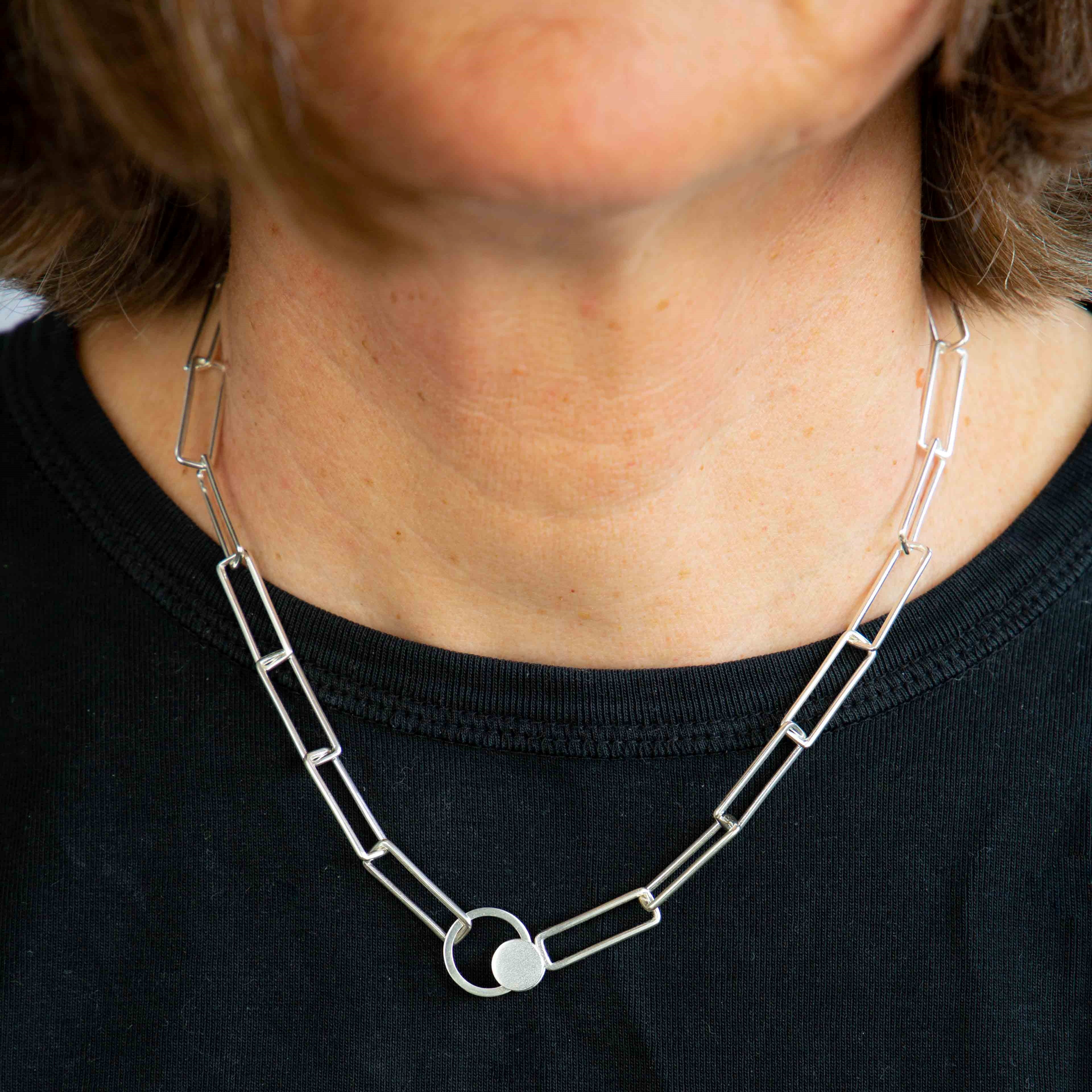 Silver necklace with rectangular links and decorative orbit feature.
